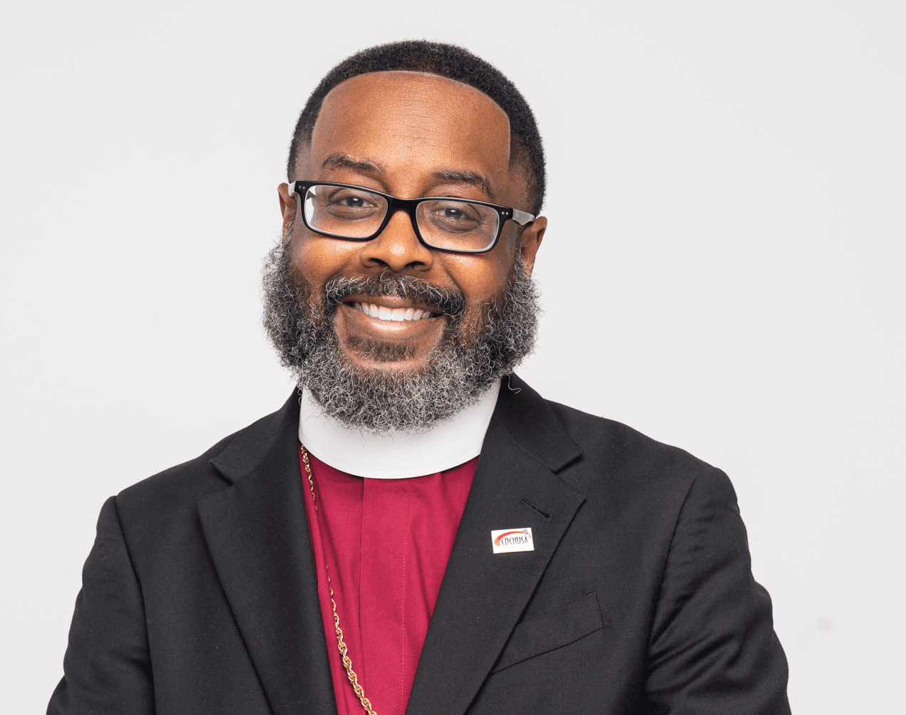Dr. Glake Hill, smiling, in clerical collar and dark suit